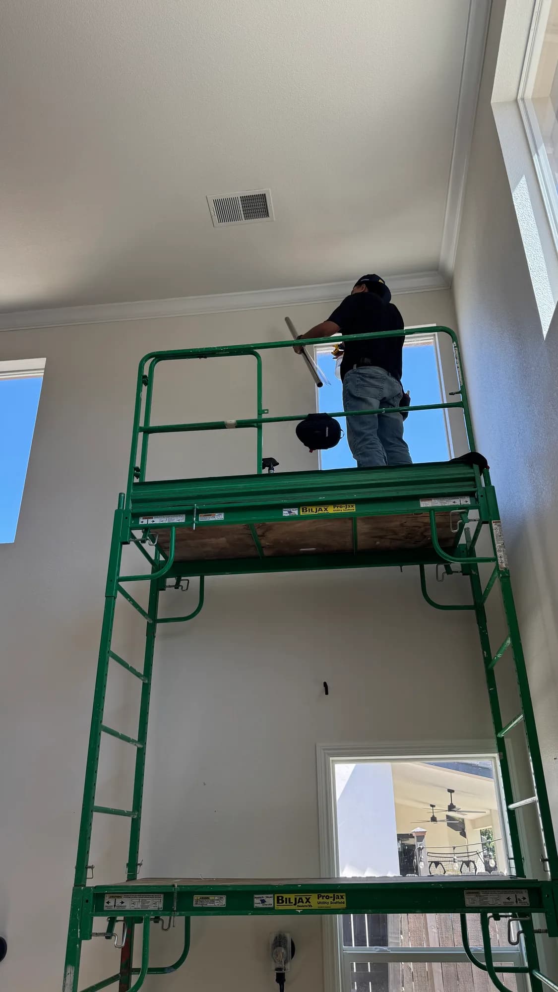 Installer on scaffolding applying window film to a high window in a two-story Ripon CA home